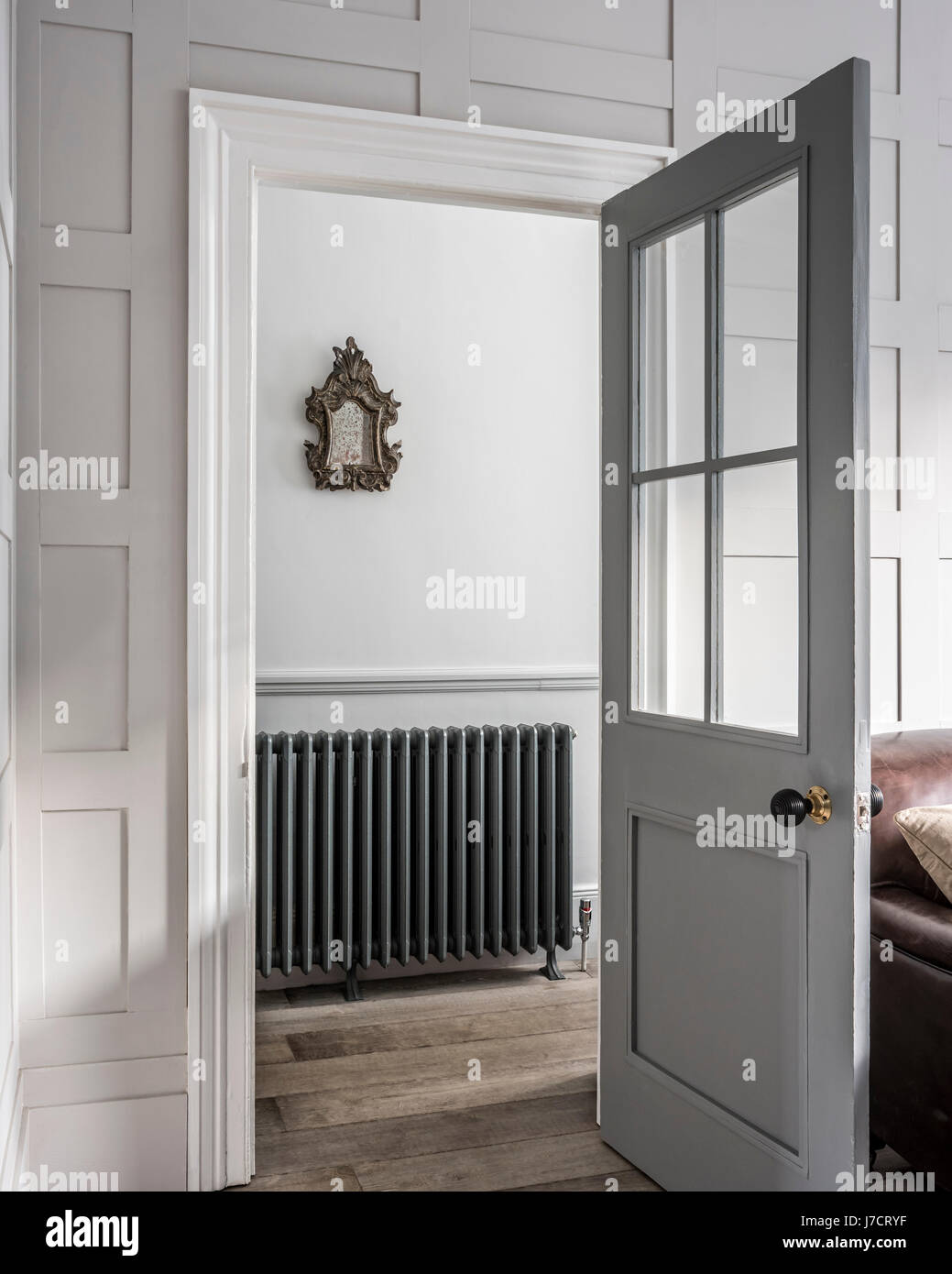 Voir par porte ouverte sur salle avec le modèle néo-classique de radiateur arroll. Un miroir doré années 1750 est suspendu au-dessus du radiateur. Banque D'Images