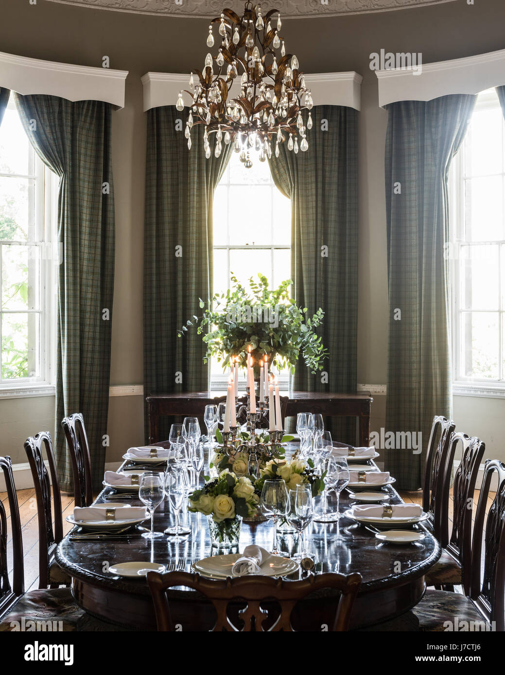 Chandelier de verre de JFM interiors au-dessus de table à manger pour un repas officiel avec des eucalyptus et des roses blanches. La longueur de plancher ar rideaux Banque D'Images