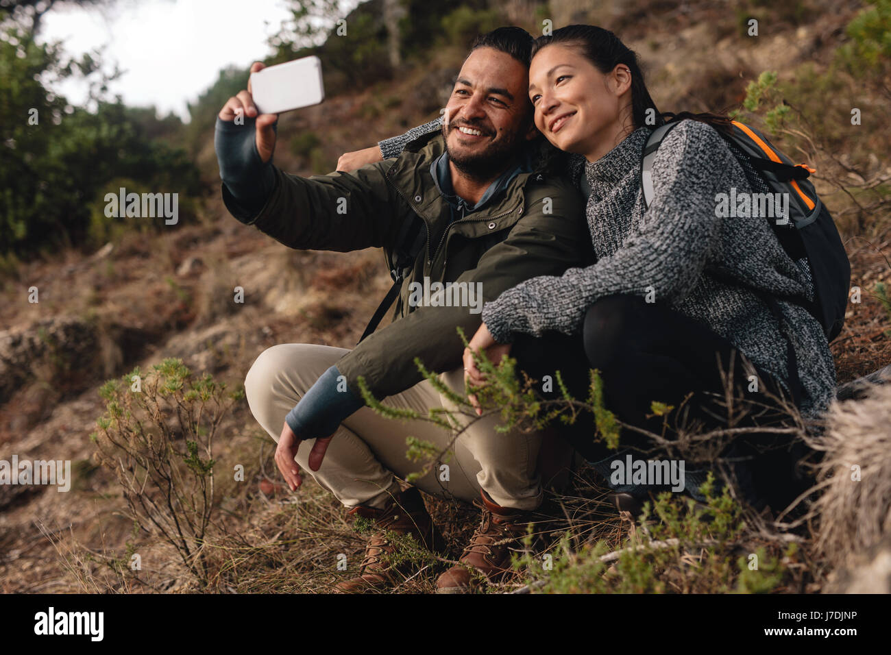 Couple amoureux assis sur sentier de montagne et prendre. selfies Young man and woman hiking in countryside et parler self portrait avec téléphone mobile. Banque D'Images