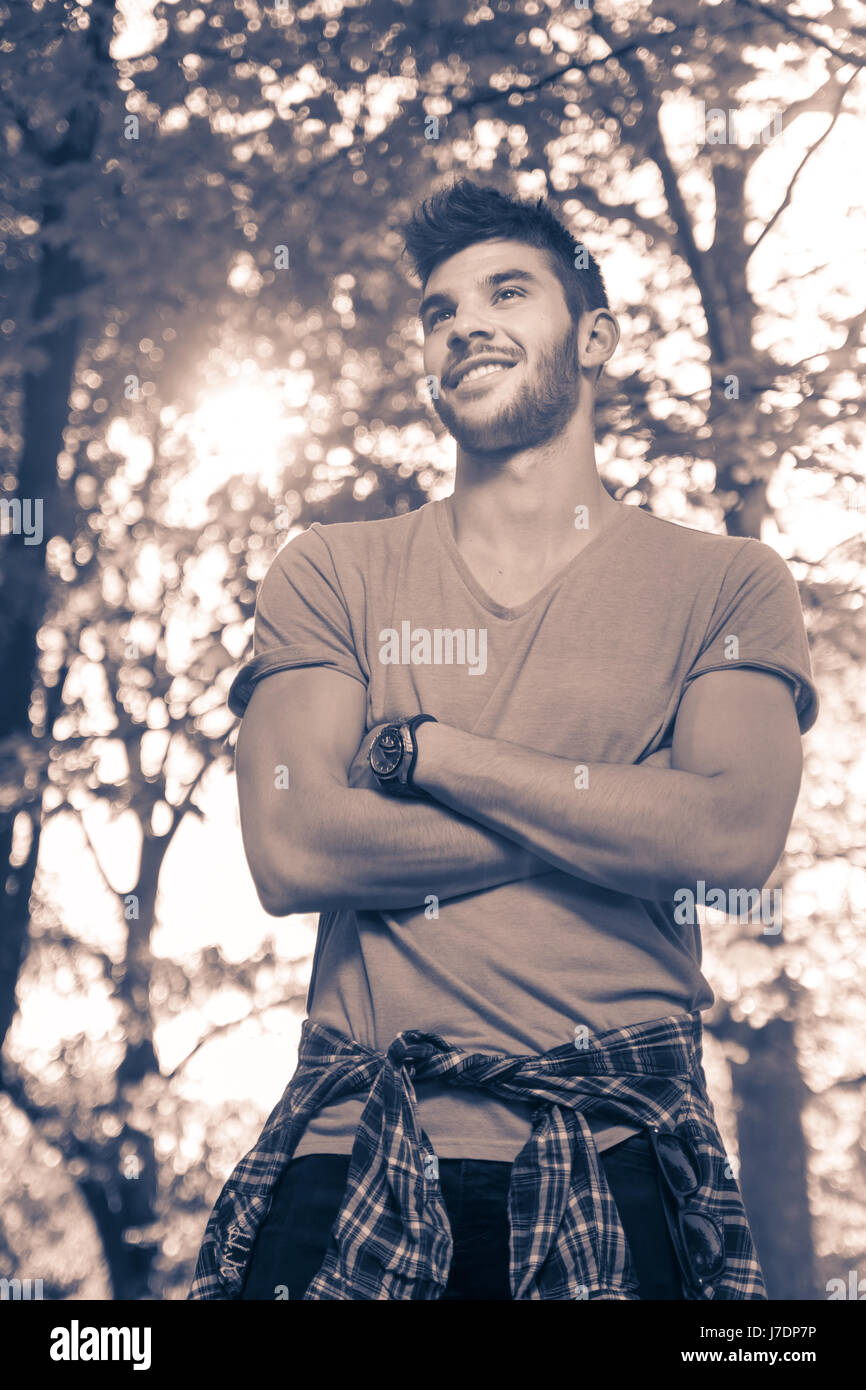 Un jeune homme, souriant, haut du corps tourné, dehors parc nature des branches d'arbre, journée ensoleillée, duotone, image en noir et blanc Banque D'Images