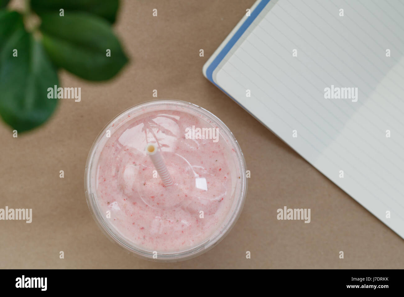 Vue de dessus d'un smoothie aux fraises dans une tasse en plastique avec une paille sur la table avec un ordinateur portable. L'été et de vie sain concept. Banque D'Images