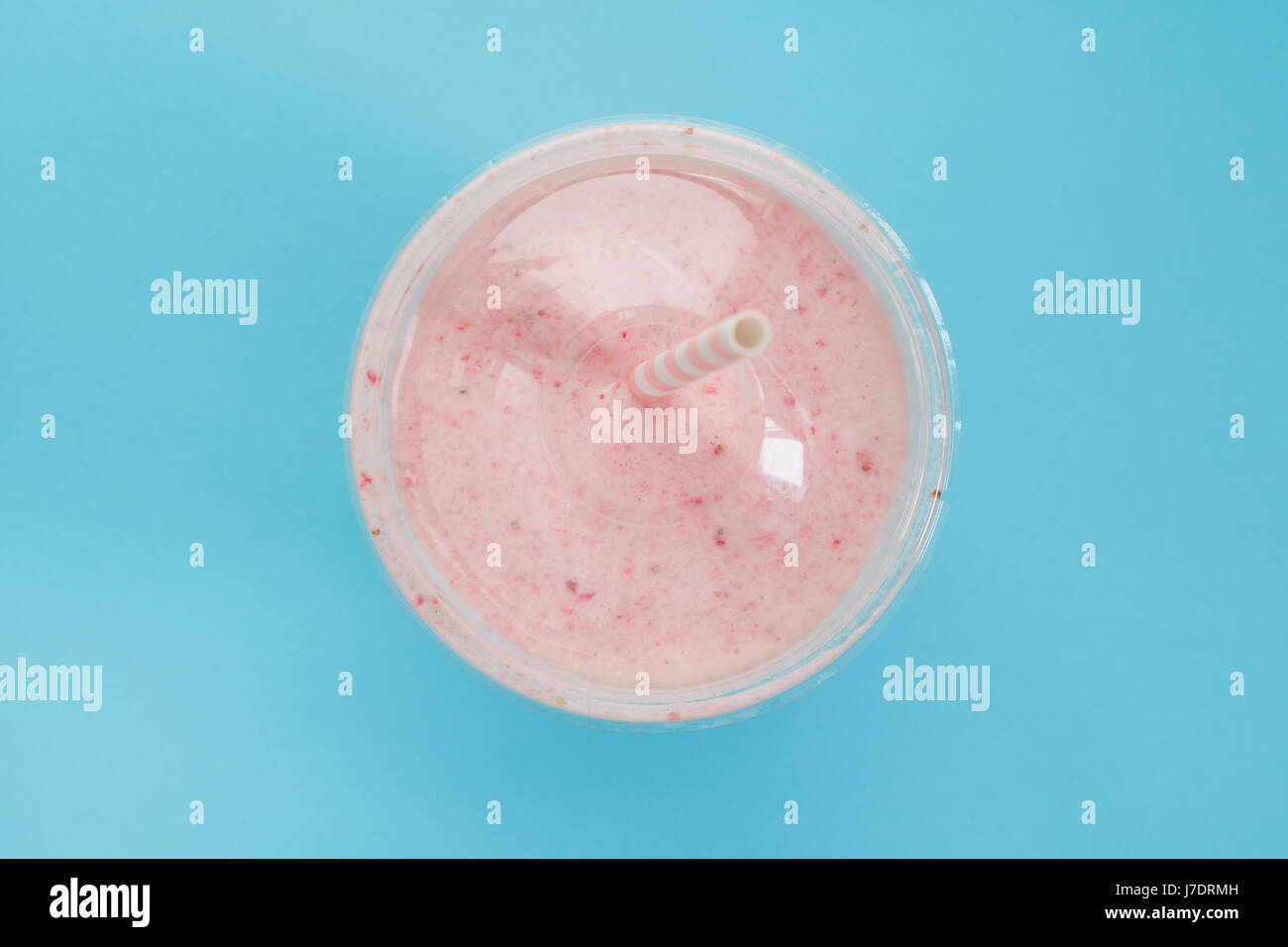 Vue de dessus d'un smoothie aux fraises dans une tasse en plastique avec une paille sur fond bleu. Couleur pastel. L'été et de vie sain concept. Banque D'Images