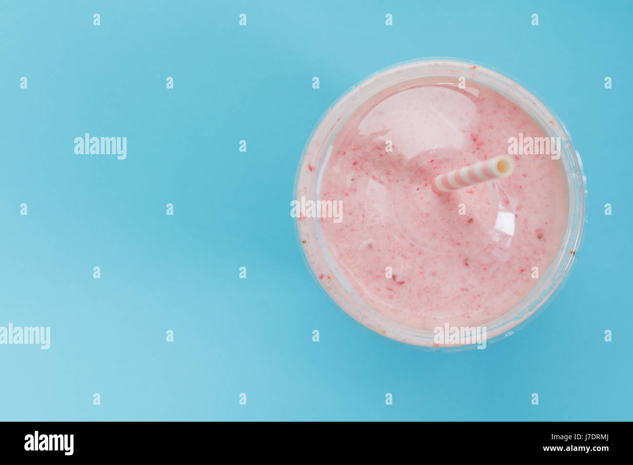 Vue de dessus d'un smoothie aux fraises dans une tasse en plastique avec une paille sur fond bleu. Couleur pastel. L'été et de vie sain concept. Banque D'Images