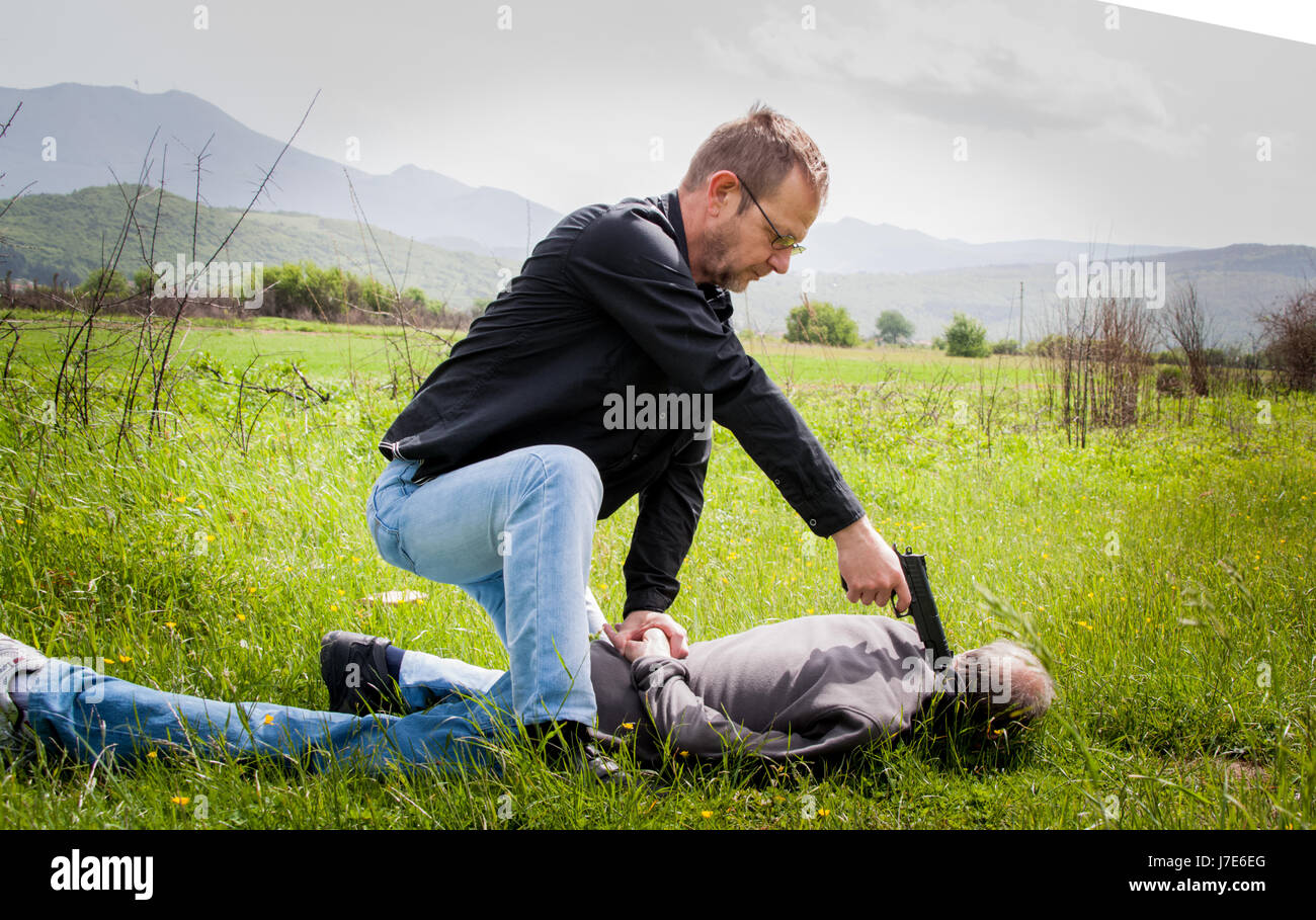 La scène du crime, le meurtre, l'enquête, la police pris le tueur et détenu, killer couché dans l'herbe, les mains derrière le dos, cop avec Banque D'Images