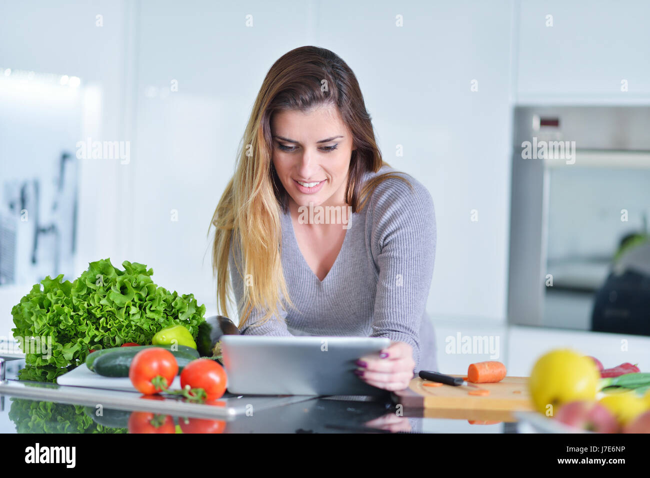 Jeune femme fait des achats en ligne par l'ordinateur tablette. Femme au foyer trouvés nouvelle recette pour la cuisine dans une cuisine Banque D'Images
