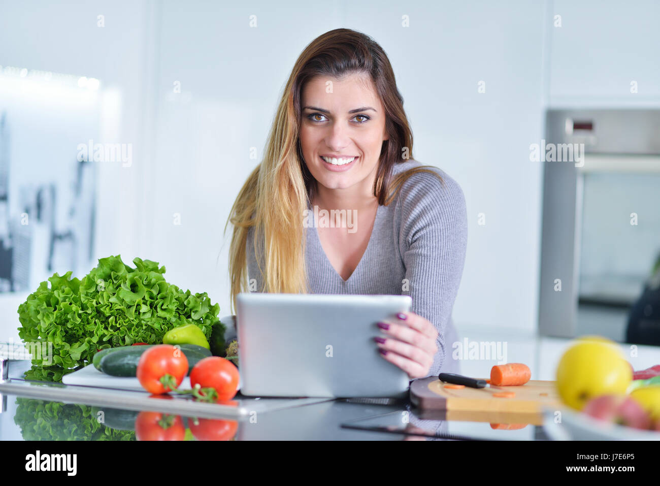 Jeune femme fait des achats en ligne par l'ordinateur tablette. Femme au foyer trouvés nouvelle recette pour la cuisine dans une cuisine Banque D'Images