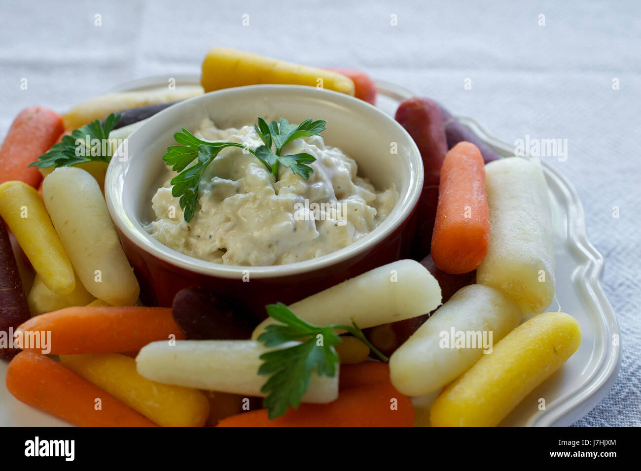 Gros plan sur assiette de carottes arc-en-ciel bébé blanc sur plaque sur nappe blanche, servi avec trempette à l'oignon yaourt grec Banque D'Images