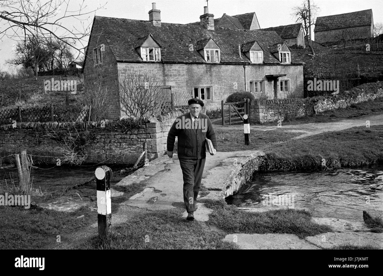 Man la livraison de journaux dimanche matin 1970 UK. La vie du village des Cotswolds. La rivière Eye passerelle. Abattage inférieure et supérieure sont deux villages sur la rivière et l'Œil sont connu comme l'Abat. 1975 HOMER SYKES Banque D'Images