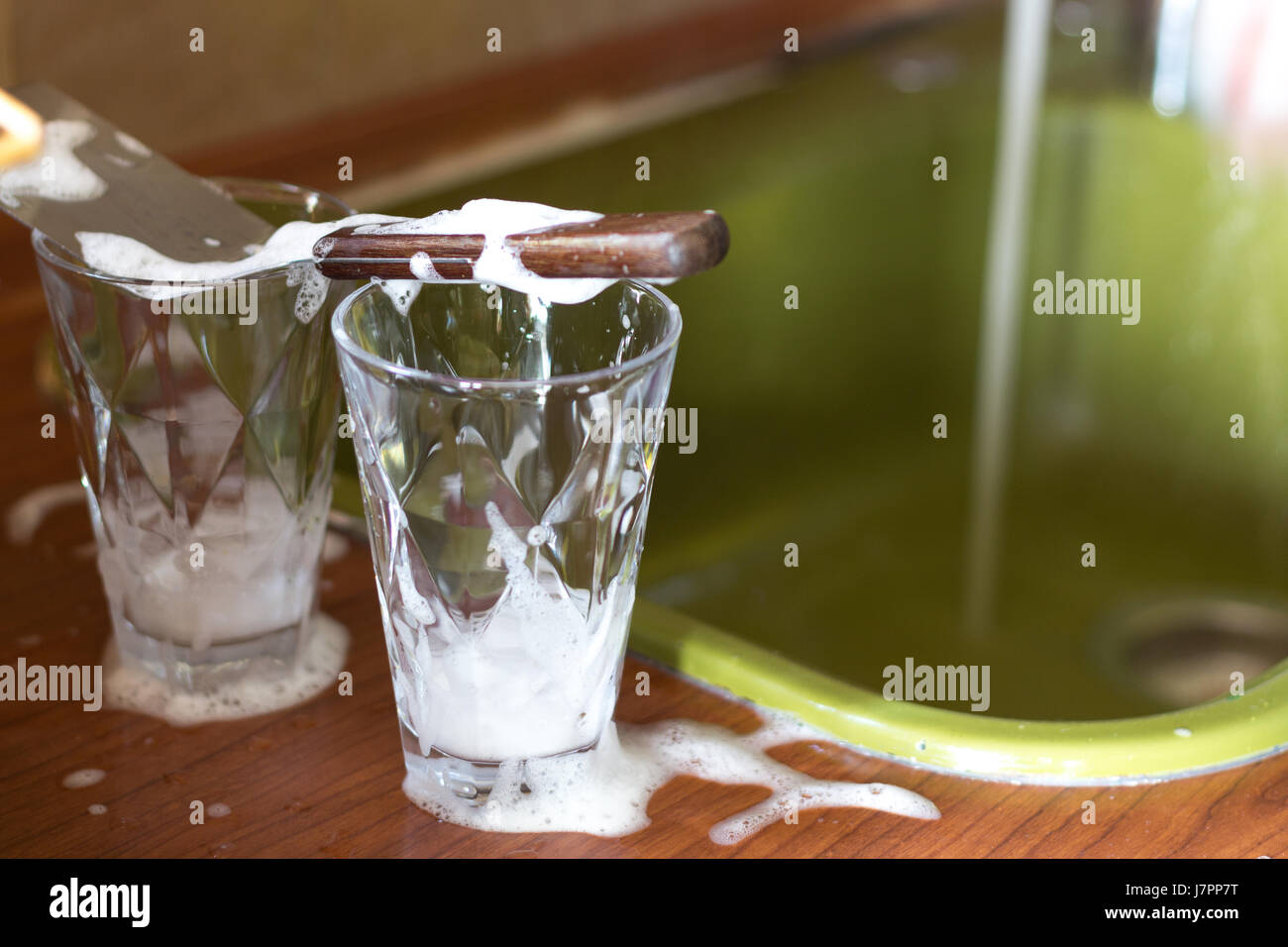 Deux verres transparents avec un détergent prêt à être lavés sur un évier de cuisine avec un écoulement de l'eau de robinet de flou en arrière-plan. Banque D'Images