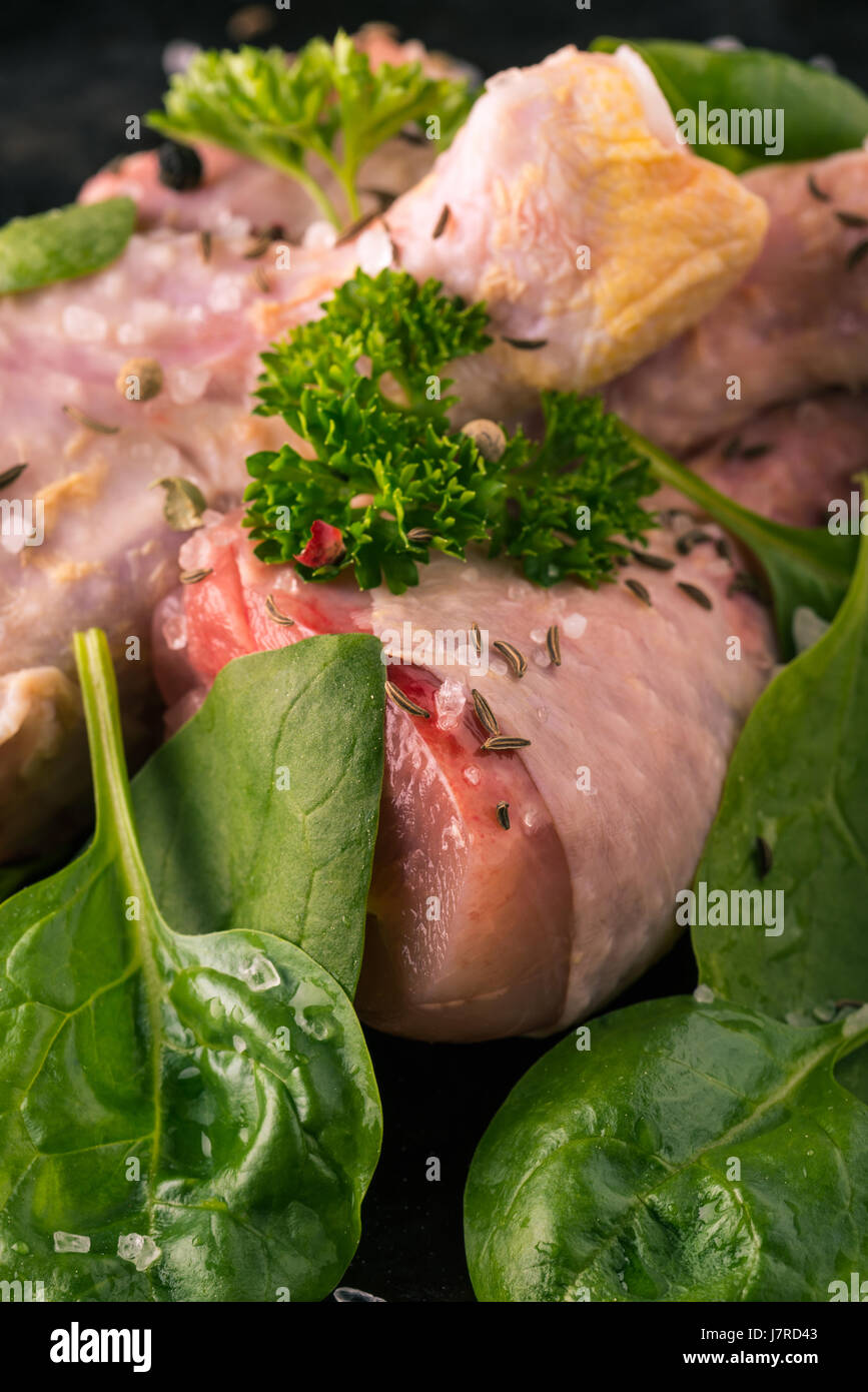 Photo verticale de cuisses de poulet cru. Trois morceaux de viande sont placés sur Dark vintage Vert bac herbes comme le persil et les épinards sont déversées autour avec Banque D'Images