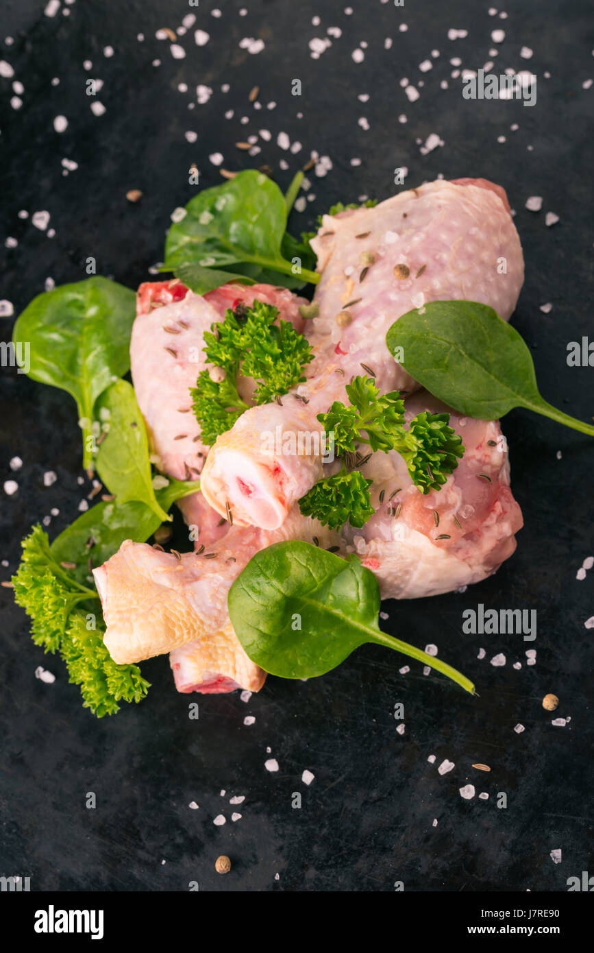 Photo verticale de cuisses de poulet cru. Trois morceaux de viande sont placés sur Dark vintage Vert bac herbes comme le persil et les épinards sont déversées autour avec Banque D'Images