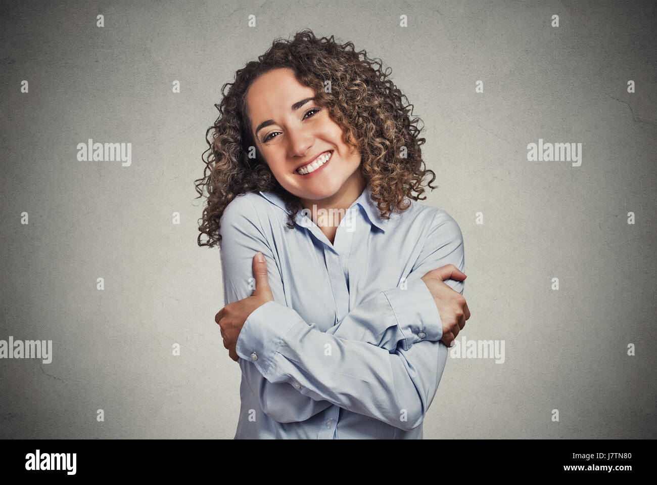 Closeup portrait confiant smiling woman holding hugging elle-même mur gris isolé arrière-plan. L'émotion positive, expression du visage, sensation, re Banque D'Images