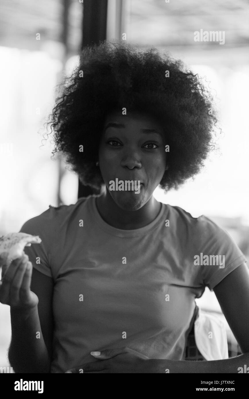 Très jeune hangry african american woman with afro hairstyle eating pizza savoureuse tranche dans fast food restaurant Banque D'Images