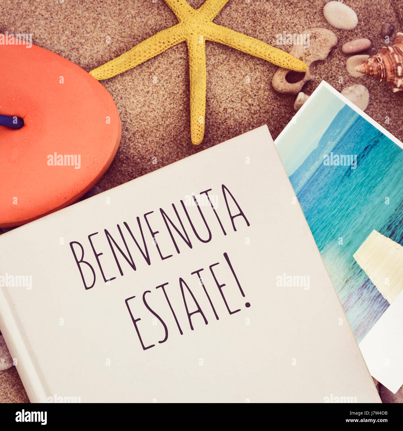 Capture d'un grand angle d'un livre avec le texte benvenuta estate, bienvenue l'été écrit en italien d'orange, une volte-face, une étoile et une photo de la mer Banque D'Images