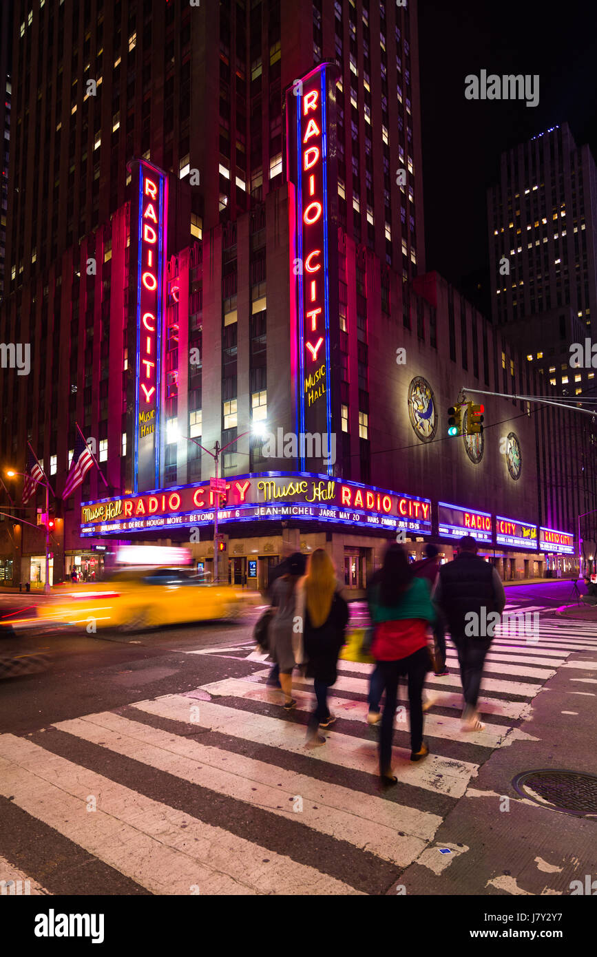 Les personnes qui traversent en direction du Radio City Music Hall de nuit avec Yellow Taxi Cab Driving passé, New York Banque D'Images