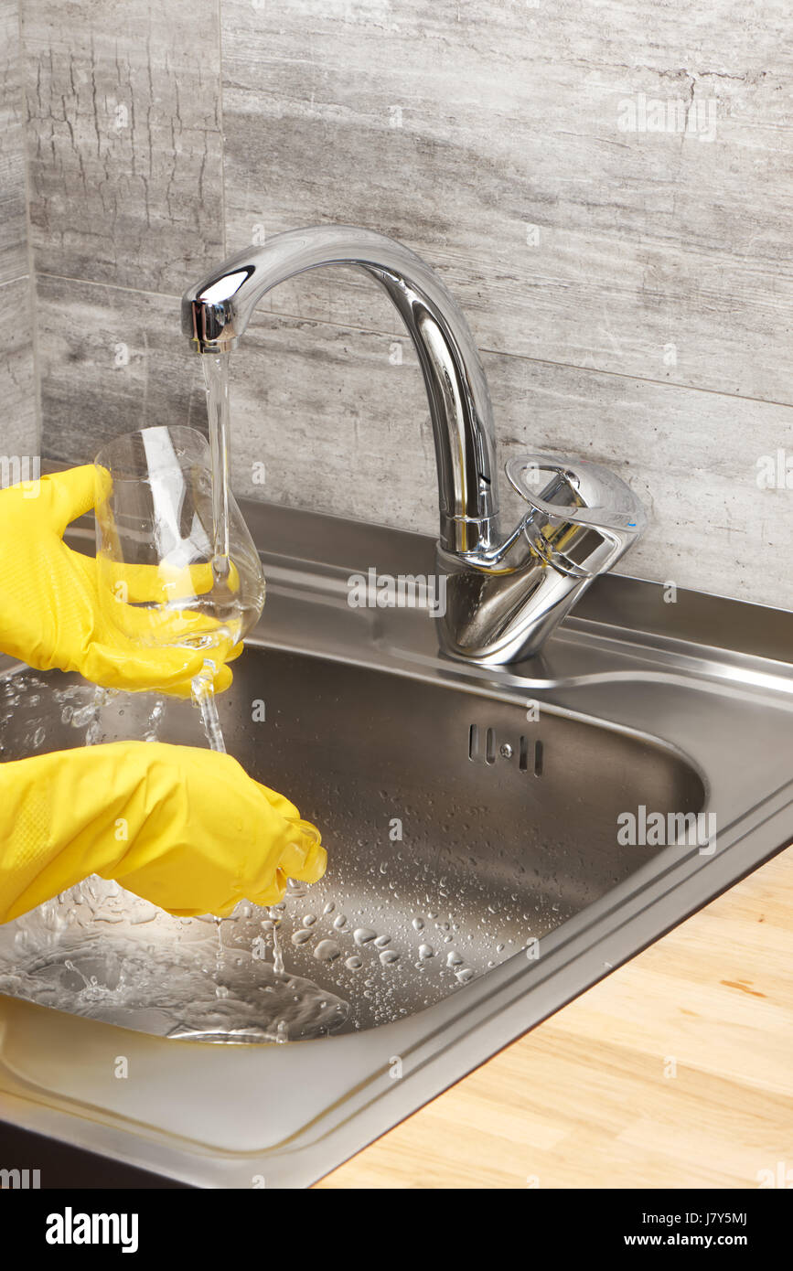 Close up de femmes dans les mains des gants en caoutchouc de protection jaune verre vin laver à l'eau courante contre l'évier de cuisine Banque D'Images