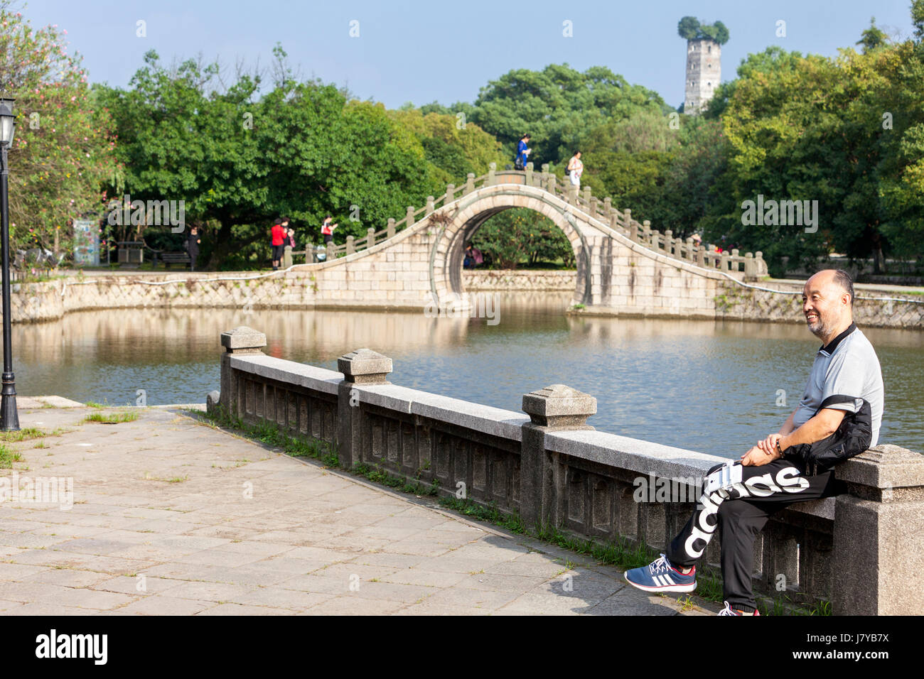 Wenzhou, Zhejiang, Chine. L'Île Jiangxin. Homme d'âge moyen se faire photographier devant la lune pont. East Pagoda en arrière-plan, reconstruite 1141. Banque D'Images