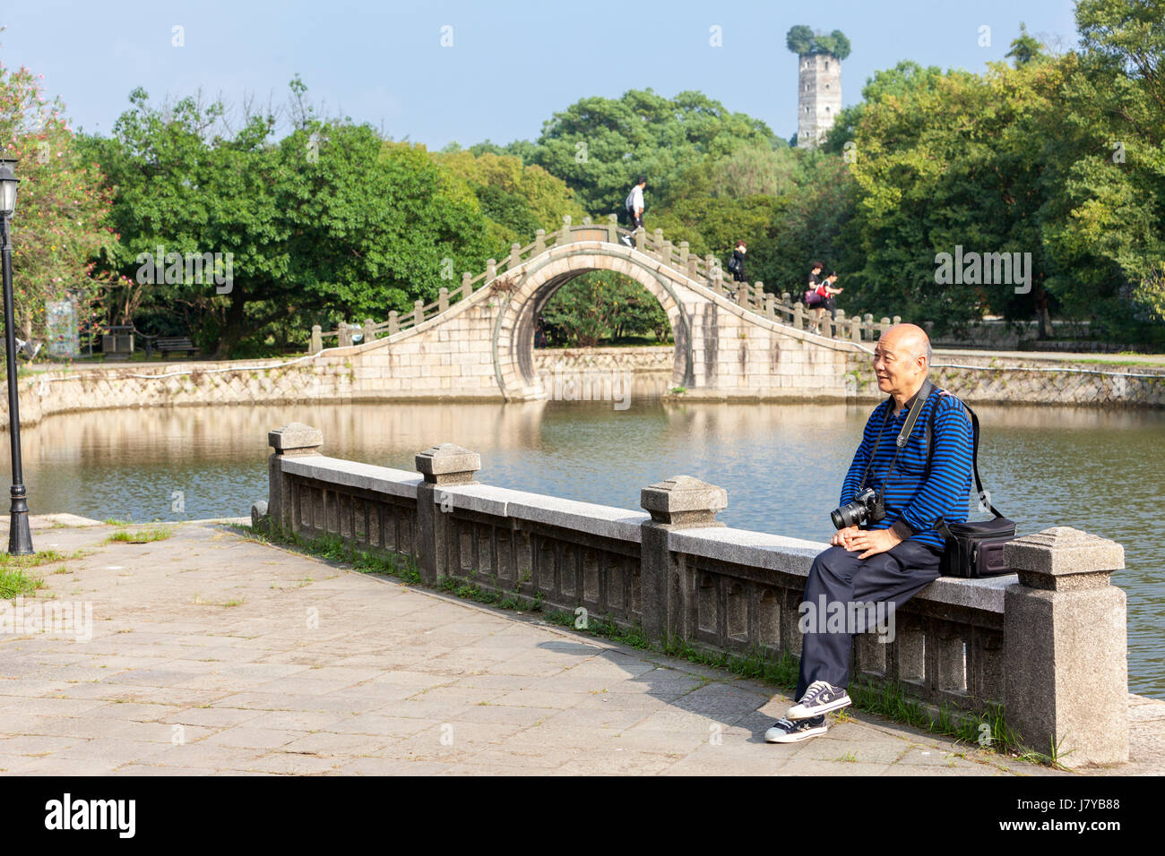 Wenzhou, Zhejiang, Chine. L'Île Jiangxin. Homme d'âge moyen se faire photographier devant la lune pont. East Pagoda en arrière-plan, reconstruite 1141. Banque D'Images