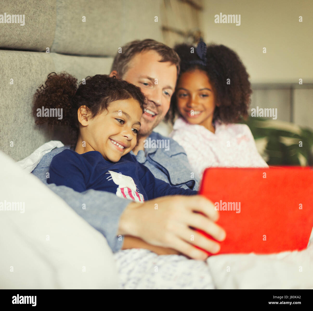 Père multi-ethnique et filles using digital tablet on bed Banque D'Images