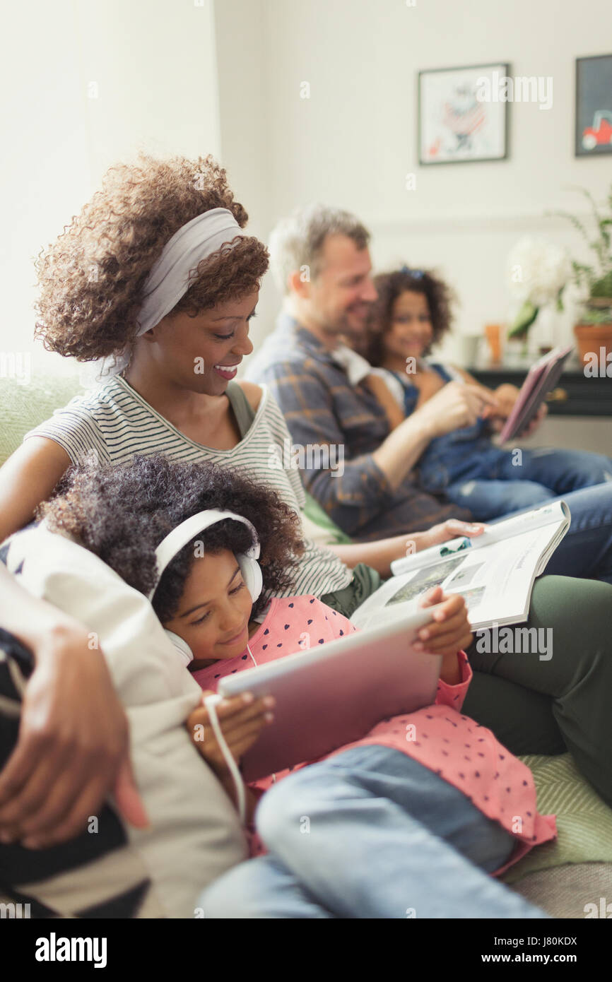 Jeune famille multi-ethnique se reposer, lire et using digital tablet on sofa Banque D'Images