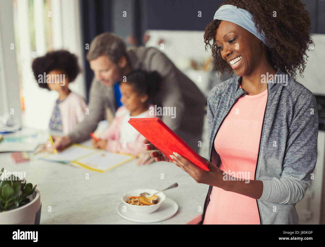 Smiling mother using digital tablet et manger le petit déjeuner dans la cuisine avec jeune famille Banque D'Images