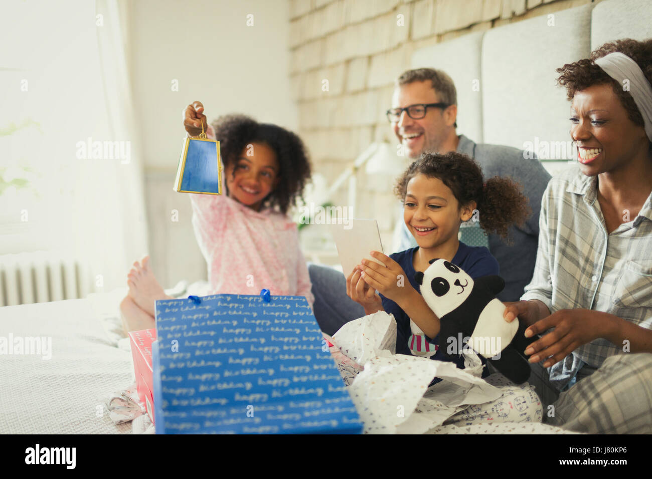 Multi-ethnic family opening birthday gift on bed Banque D'Images