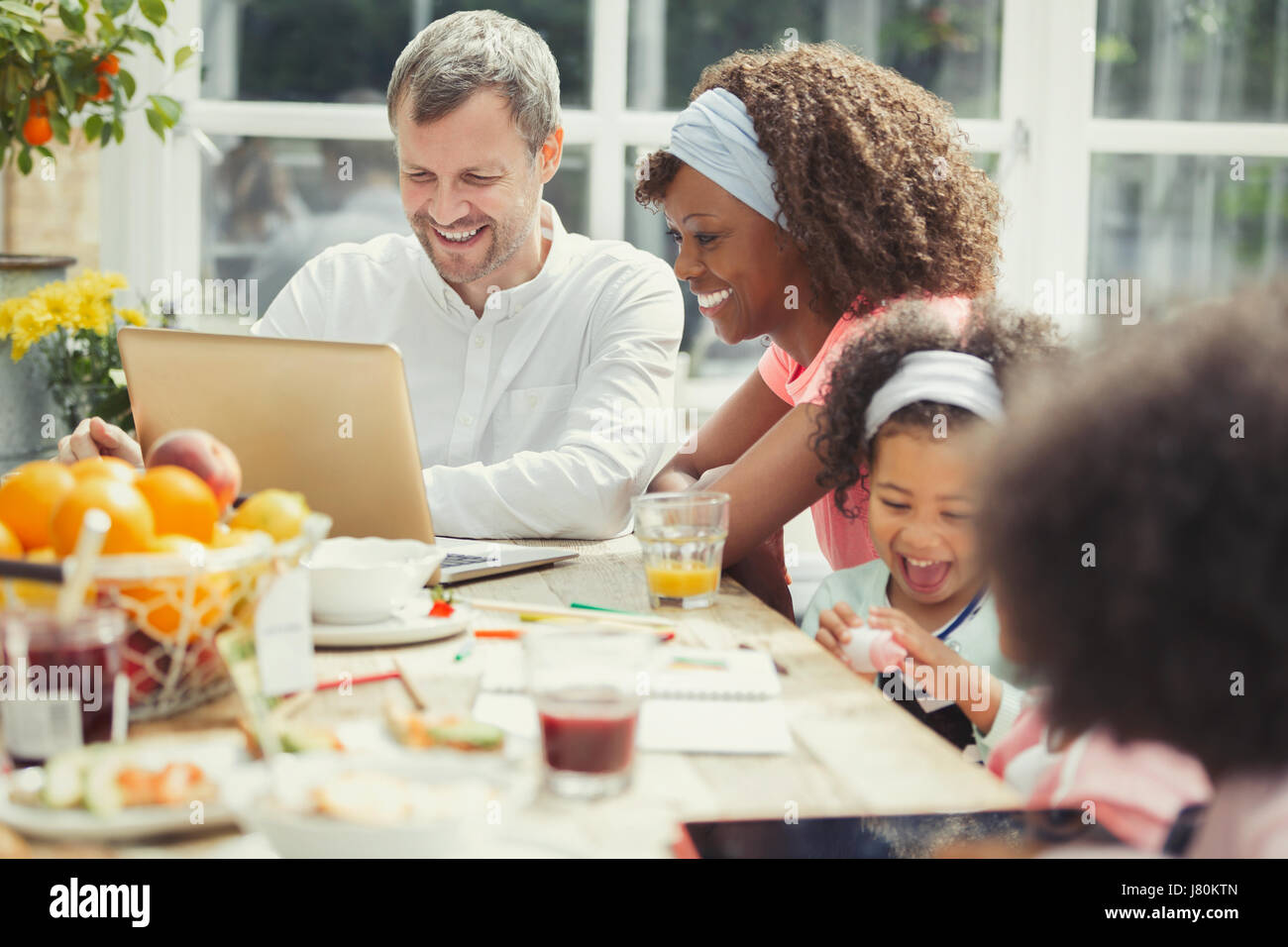 Smiling young multi-ethnic family using laptop et manger le petit déjeuner à table Banque D'Images