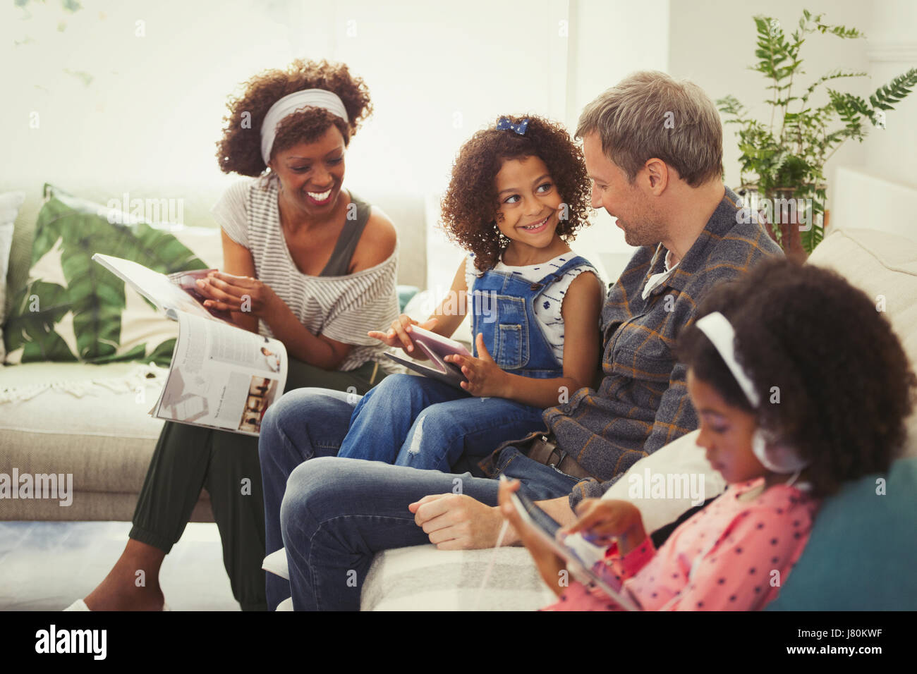 Jeune famille multi-ethnique à l'aide de tablettes numériques et lecture magazine sur canapé Banque D'Images
