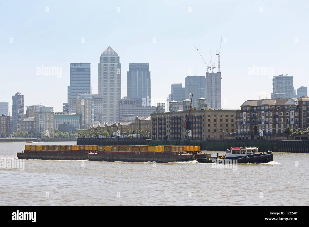 Un remorqueur des chalands, barges contenant des déchets ménagers le long de la Tamise à Londres, au Royaume-Uni. Canary Wharf à l'arrière-plan Banque D'Images