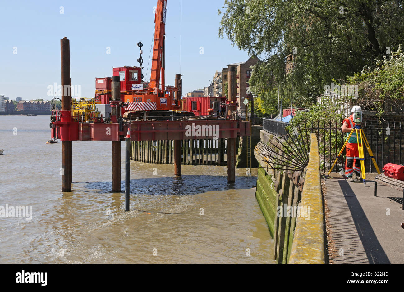 Une plate-forme de barge sur la Tamise à l'Est de Londres s'engage à travailler pour le projet de tunnel Thames Tideway. Un géomètre travaille sur la rive du fleuve (à droite) Banque D'Images