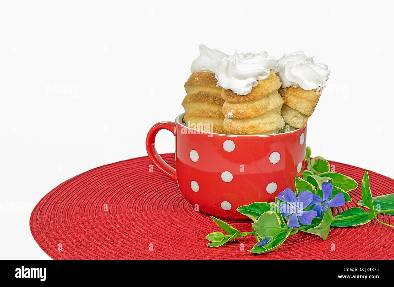 Corne crème pâtisserie dans polka dot tasse avec fleur de myrte sur place ronde rouge mat Banque D'Images