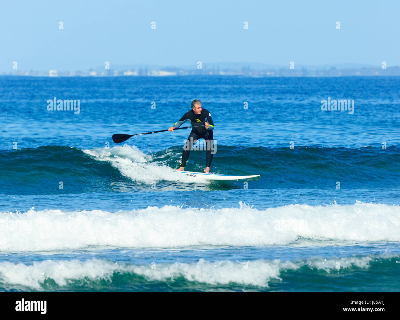 Homme 50-60 surfant sur un stand up paddleboard et porter une combinaison isothermique, 7 Mile Beach, Gerroa, New South Wales, NSW, Australie Banque D'Images