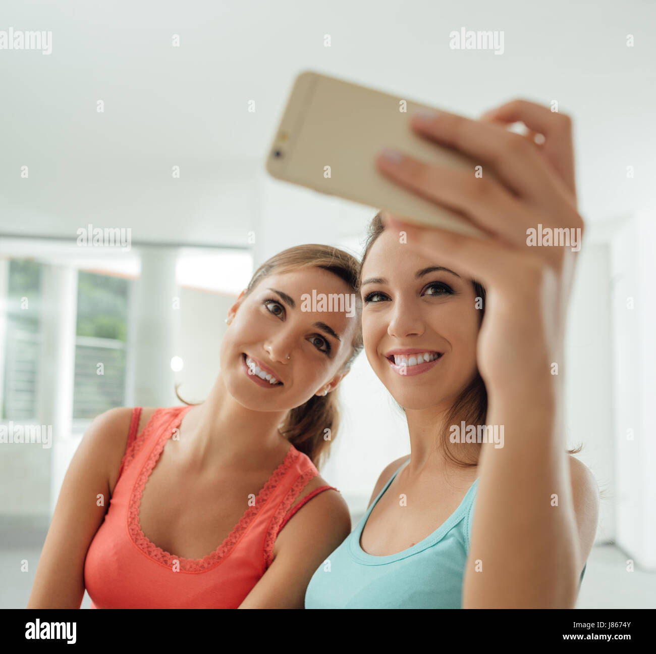 Jolies filles assis à un bureau et prendre l'autoportrait à l'aide d'un téléphone intelligent, ils sont smiling at camera et posing Banque D'Images
