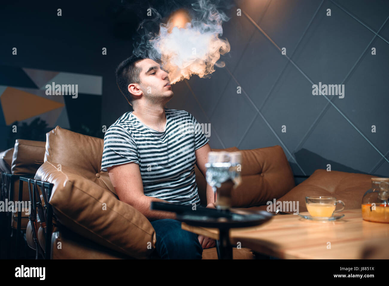 Jeune homme fumeurs et de détente au bar à narguilé. La fumée du tabac, vie nocturne Banque D'Images
