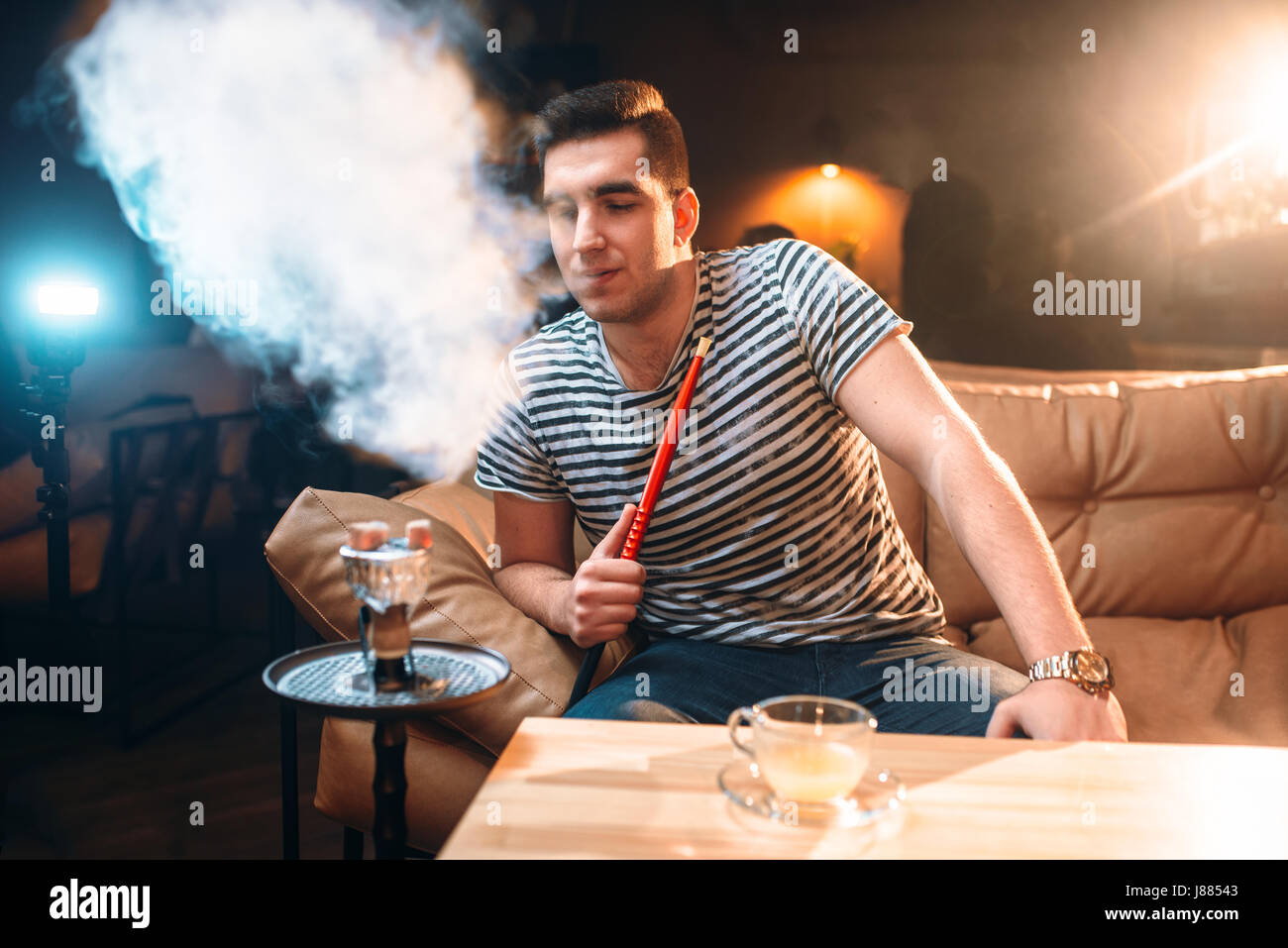 Jeune homme fumeurs et de détente au bar à narguilé. La fumée du tabac, vie nocturne Banque D'Images