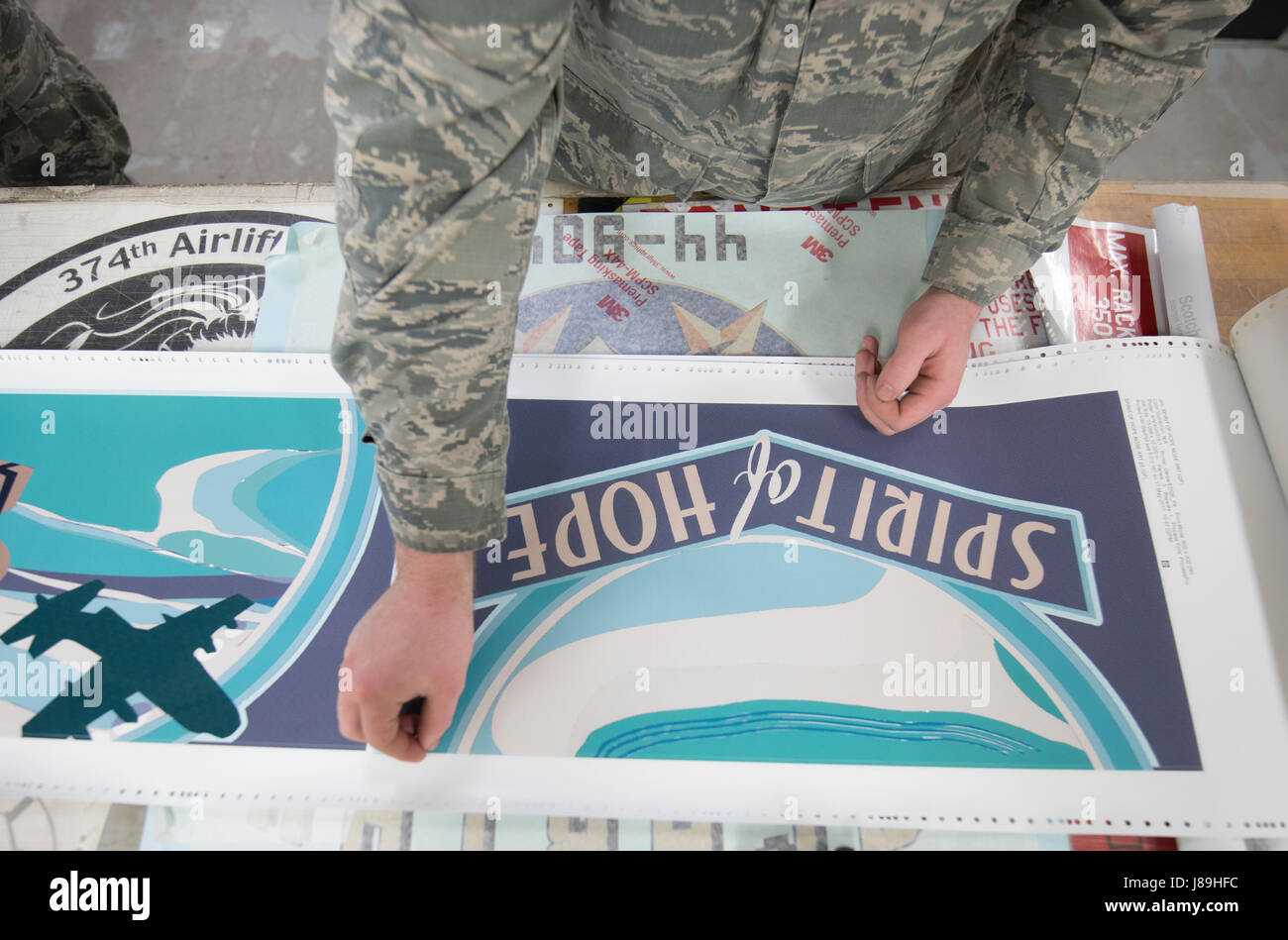 Navigant de première classe Caleb Cauthorn, 374e Escadron de maintenance Maintenance de structures d'aéronefs de compagnon, délicatement élimine l'excès de vinyle imprimé un nouveau nez pièce d'art pour un C-130J Super Hercules à Yokota Air Base, Japon, le 19 mai, 2017. Le nez l'art est imprimé sur vinyl de sélectionner les membres de l'atelier et soigneusement appliquée à la surface préparée de l'avion. L'approche numérique a pris plus de 30 heures pour terminer le projet de sketch pad pour l'impression prépresse. (U.S. Air Force photo par Yasuo Osakabe) Banque D'Images