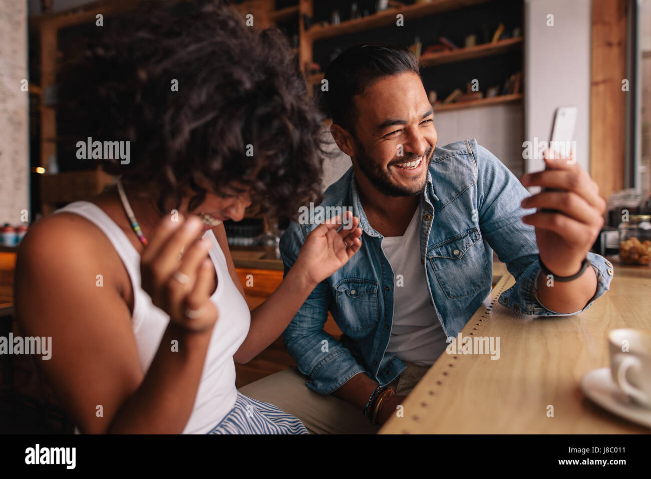 Smiling young couple sitting at coffee shop à l'aide de téléphone mobile. Jeune homme et femme à prendre café et selfies rire. Banque D'Images