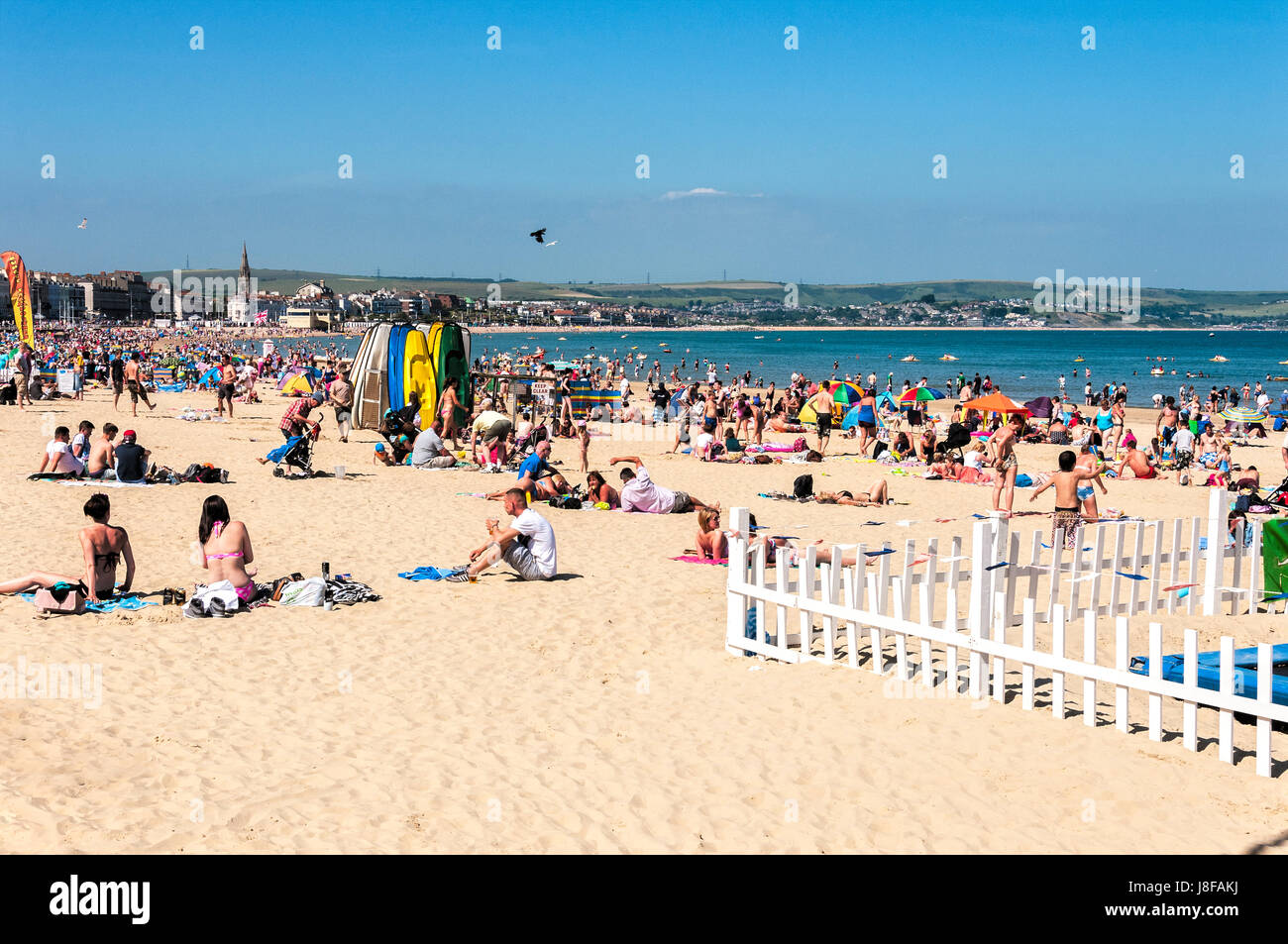 Les baigneurs et les nageurs vous détendre sur le grand strand en pente composé de lumière douce et de sable le bain dans la mer bleue à Weymouth Beach Banque D'Images