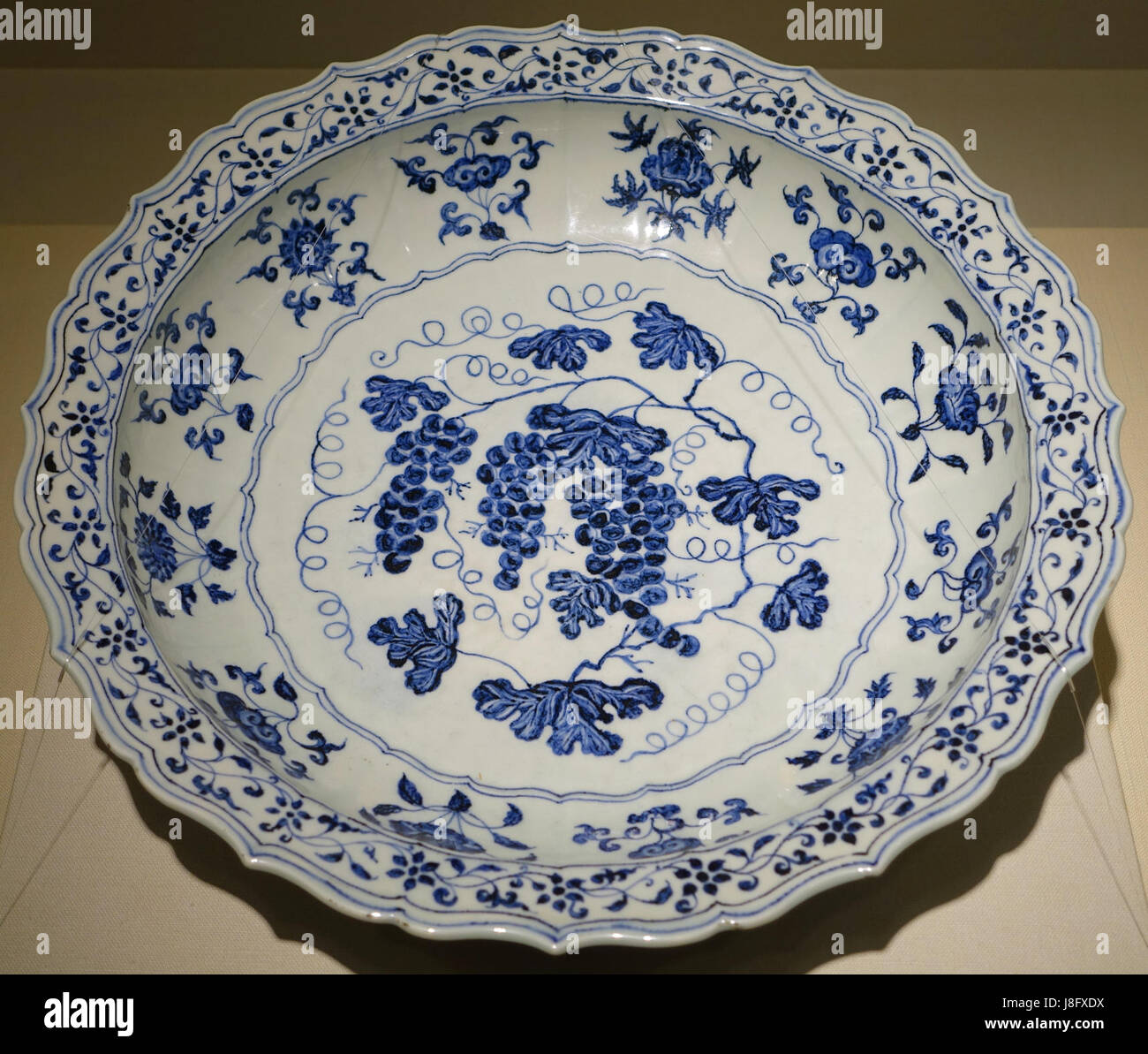 Ce grand plat bleu et blanc arbore un motif de vigne et a été produit au four de Jingdezhen en Chine pendant la dynastie Ming, période Yongle (1403-1424 AD). Il fait partie de la collection du Matsuoka Museum of Art de Tokyo, au Japon, mettant en valeur l'art complexe de la porcelaine de cette période. Banque D'Images Ce grand plat bleu et blanc arbore un motif de vigne et a été produit au four de Jingdezhen en Chine pendant la dynastie Ming, période Yongle (1403-1424 AD). Il fait partie de la collection du Matsuoka Museum of Art de Tokyo, au Japon, mettant en valeur l'art complexe de la porcelaine de cette période. Banque D'Images