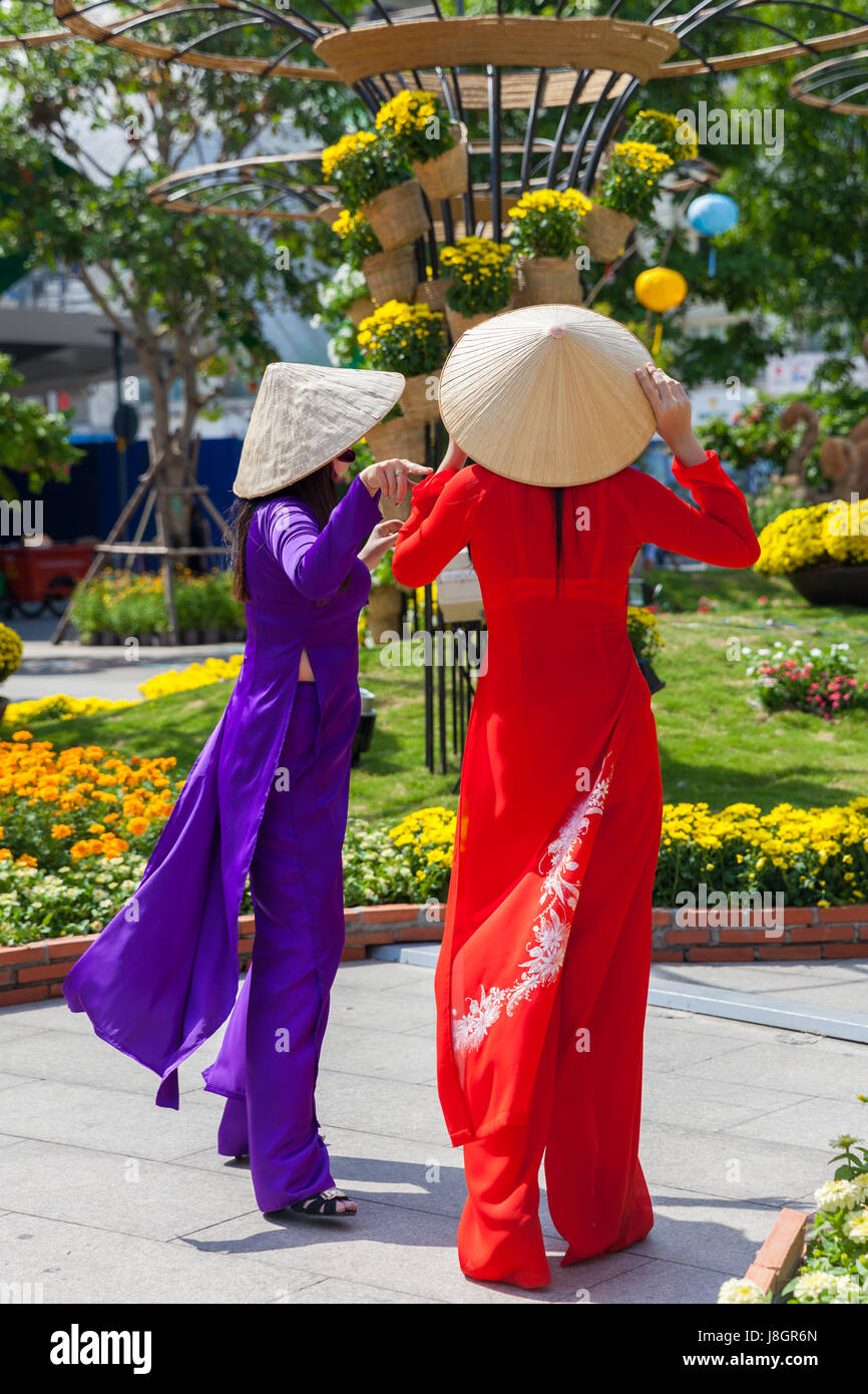 Ho Chi Minh Ville, Vietnam - Février 07, 2016 : Deux jeunes femmes vietnamiennes en robe traditionnelle Ao Dai se font passer pour des images en face de fleurs à Banque D'Images