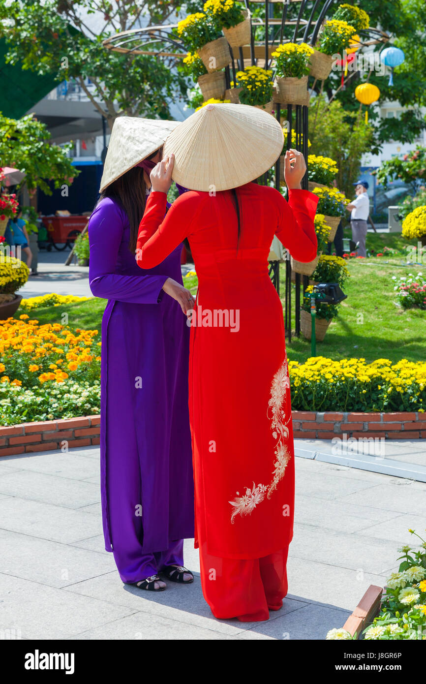 Ho Chi Minh Ville, Vietnam - Février 07, 2016 : Deux jeunes femmes vietnamiennes en robe traditionnelle Ao Dai se font passer pour des images en face de fleurs à Banque D'Images