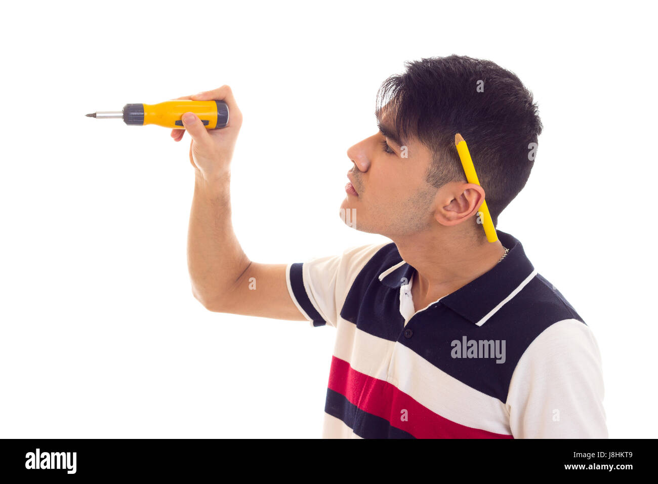 Jeune homme fort avec des cheveux noirs en blanc et bleu t-shirt avec crayon derrière l'oreille holding tournevis jaune sur fond blanc en studio Banque D'Images