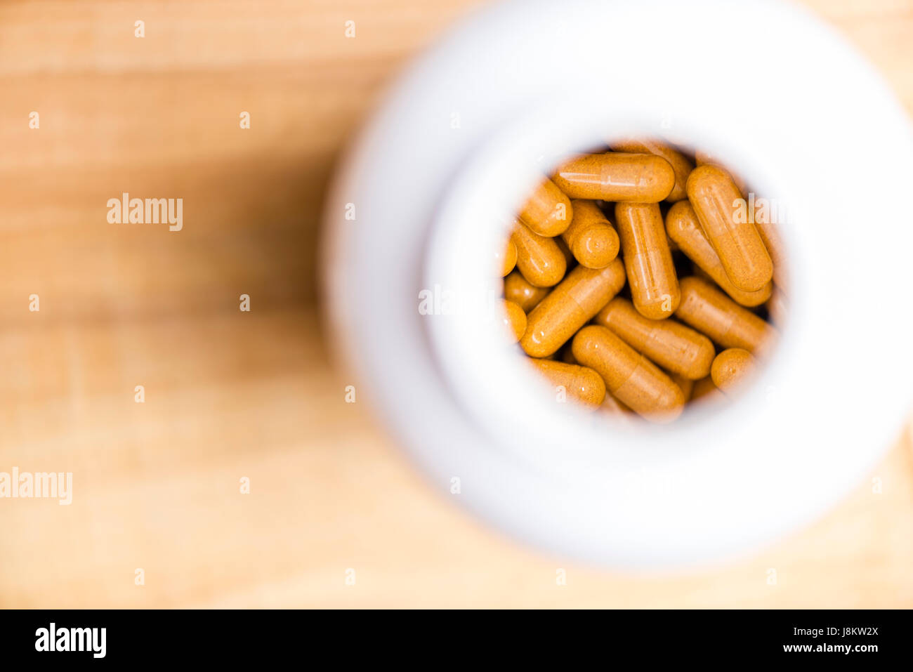 plat de capsules curcuma dans une bouteille en plastique blanc sur une table en bois Banque D'Images