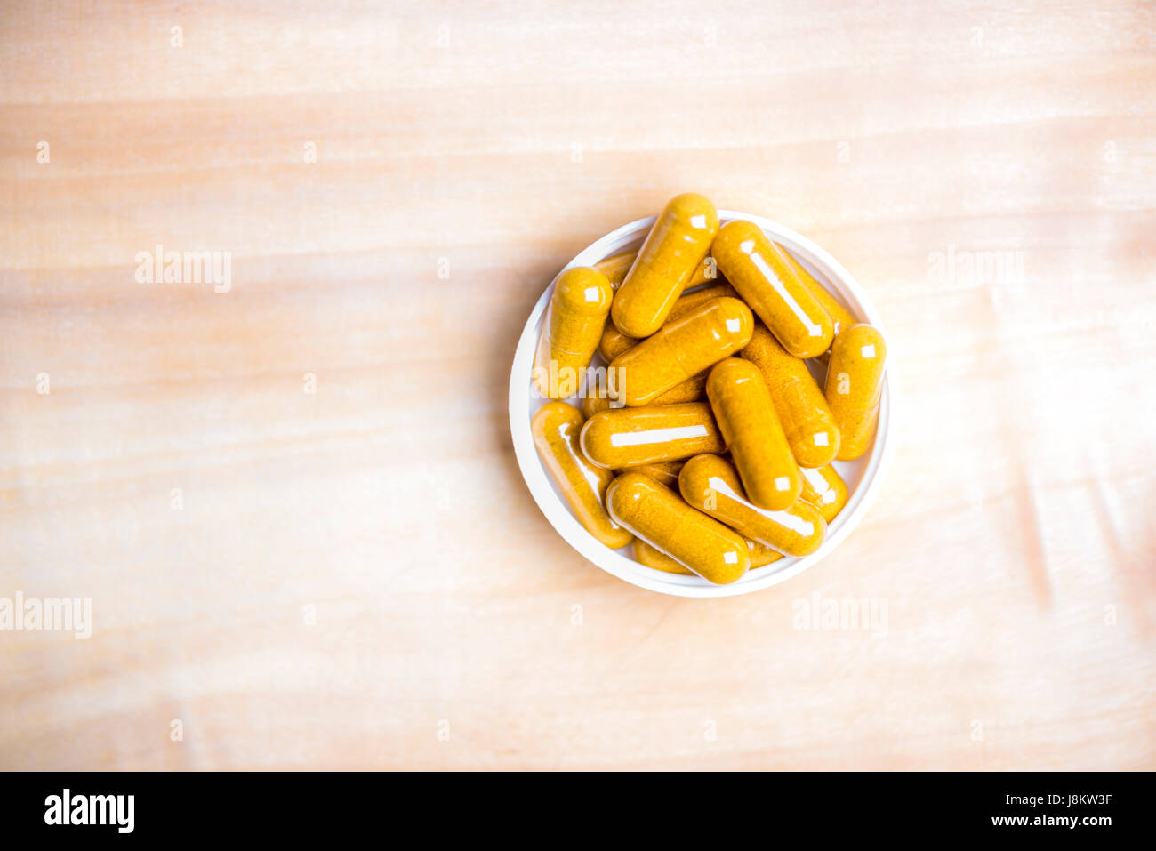 plat de capsules curcuma dans une bouteille en plastique blanc sur une table en bois Banque D'Images