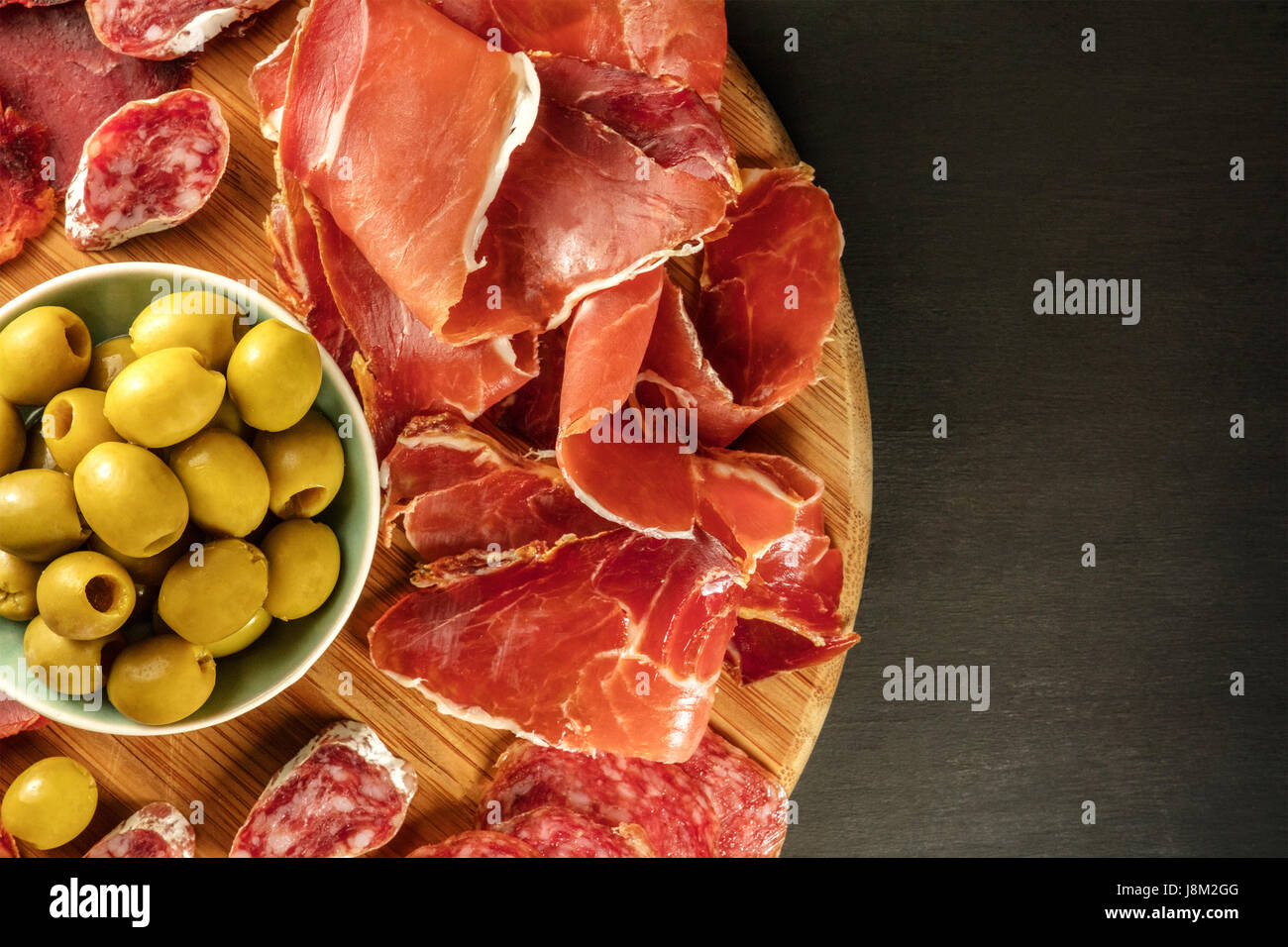 Une photo prise à la verticale d'une assiette de charcuterie espagnole avec  jambon et saucisse cafe, aux olives vertes, sur un fond sombre avec une  place pour le texte Photo Stock -