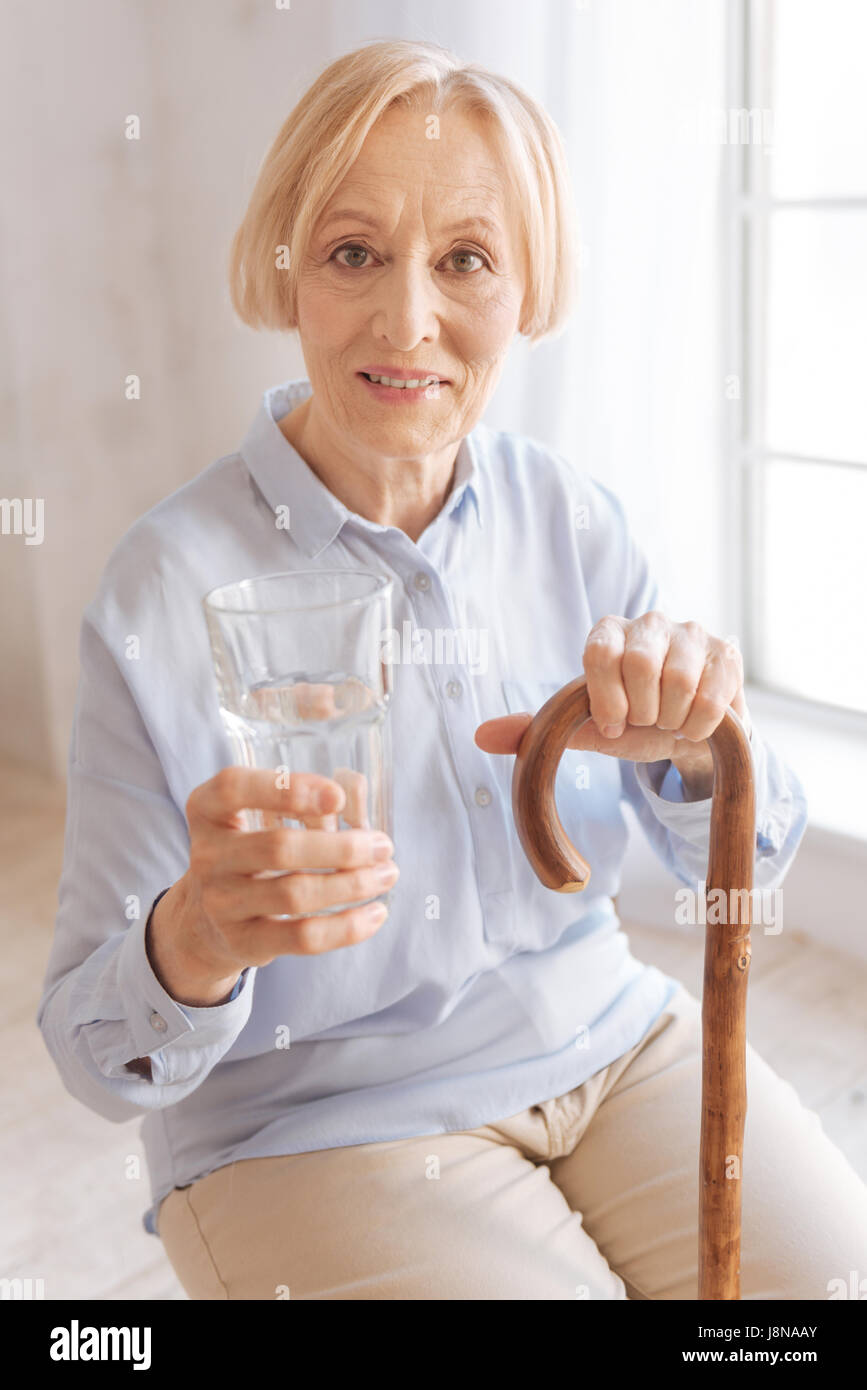 Photo de l'angle faible. Dame mature se froisser son front en position semi assise tout en tenant une canne dans la main gauche Banque D'Images