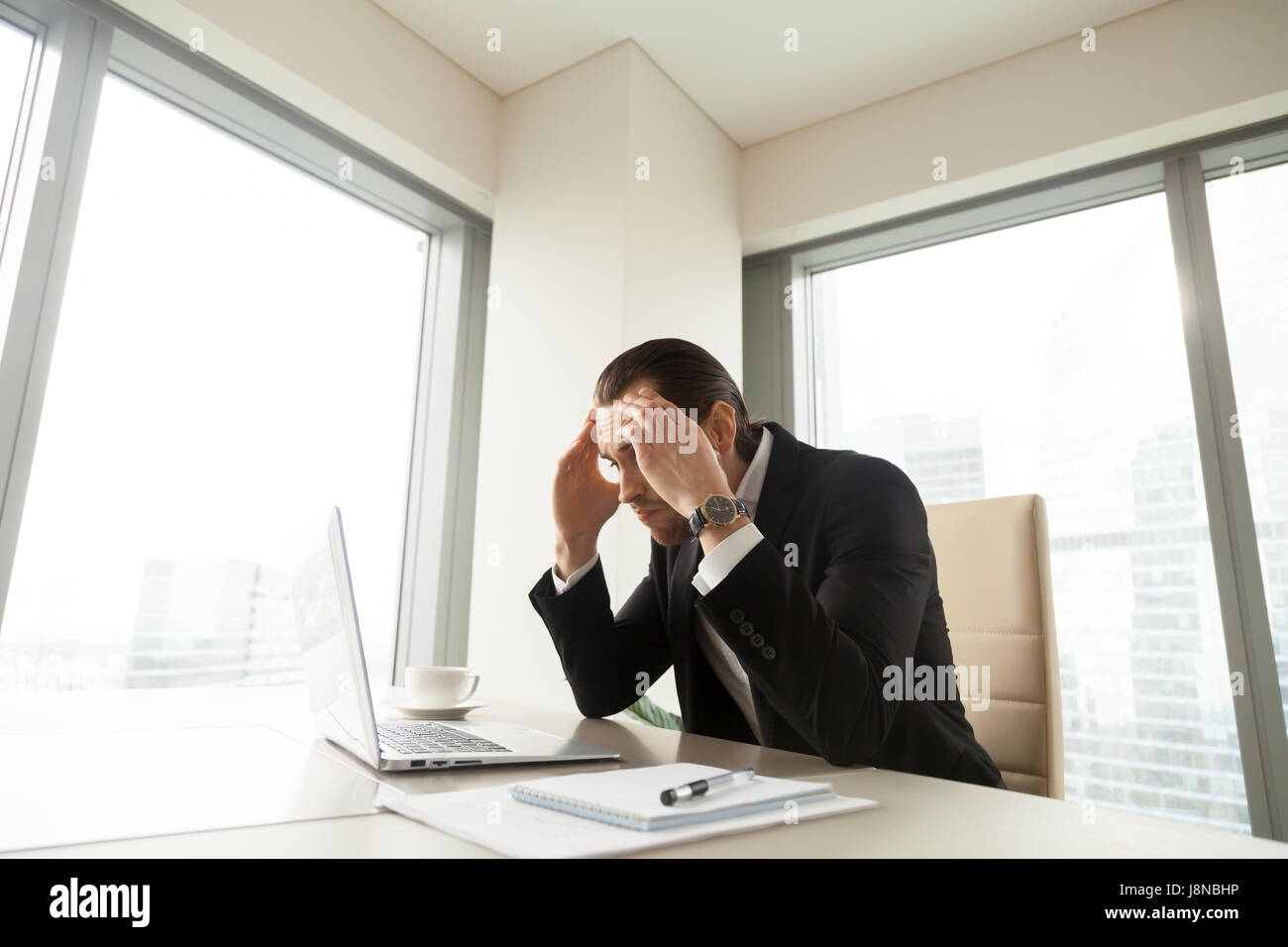 Businessman holding a souligné la tête dans les mains à la recherche sur pc l'écran du portable. Entrepreneur fatigué épuisé avec trop de temps de travail. Disque thinki exécutif Banque D'Images