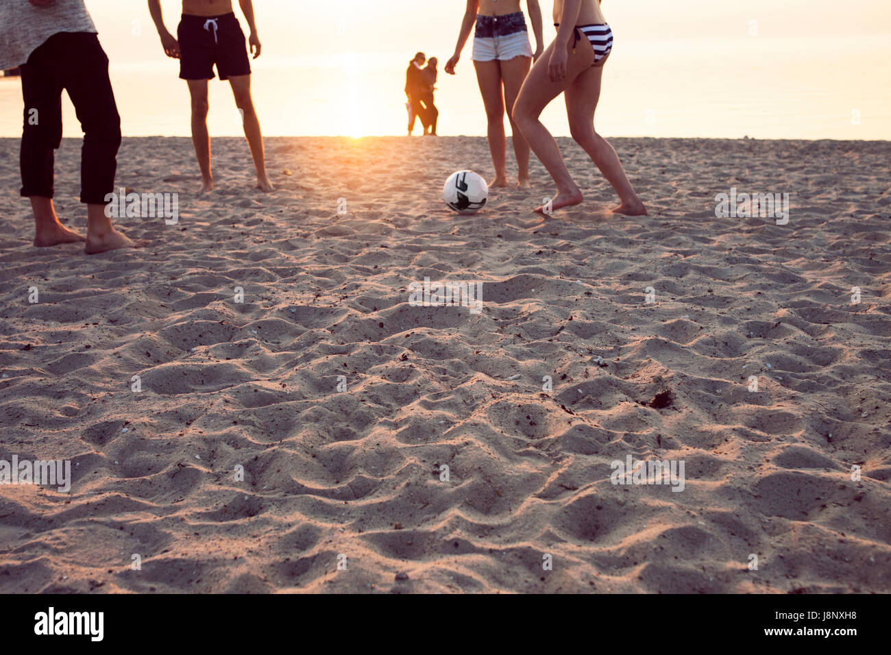 Les jeunes hommes, les jeunes femmes et teenage girl (16-17) jouant au football sur le sable au coucher du soleil Banque D'Images