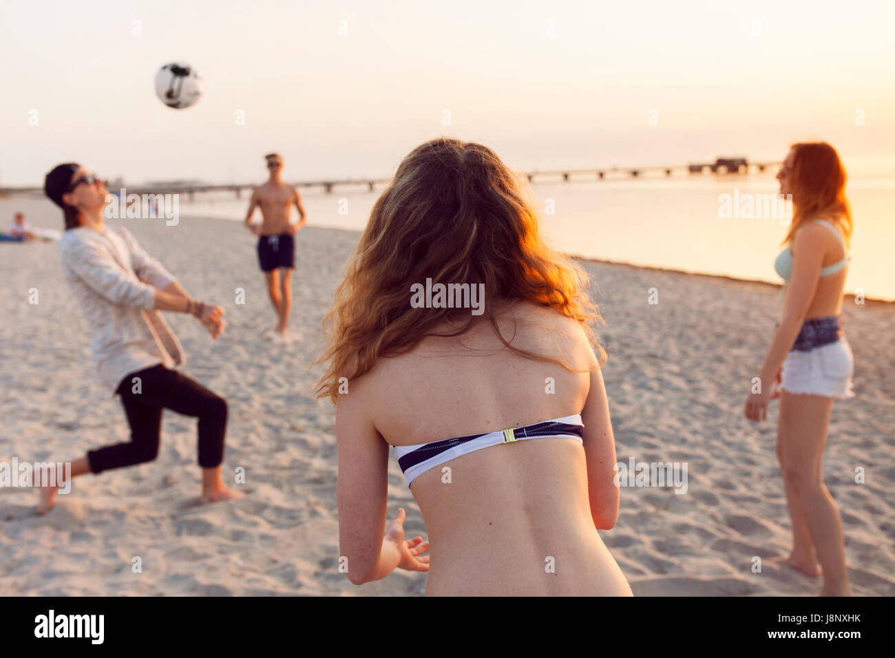 Les jeunes hommes, les jeunes femmes et teenage girl (16-17) jouer au volley-ball sur le sable au coucher du soleil Banque D'Images