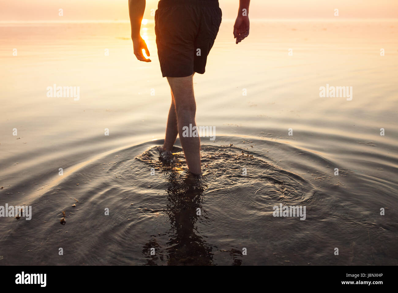 Homme en short de patauger dans la mer au coucher du soleil Banque D'Images